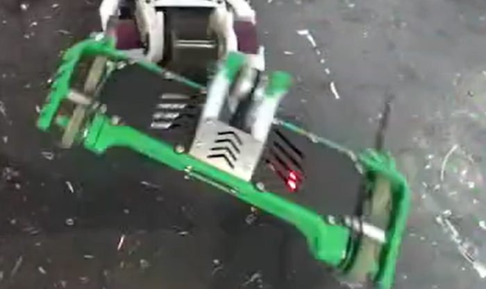 The robot tilted mid-hit, showing the chevron-marked weapon shield and red LED.